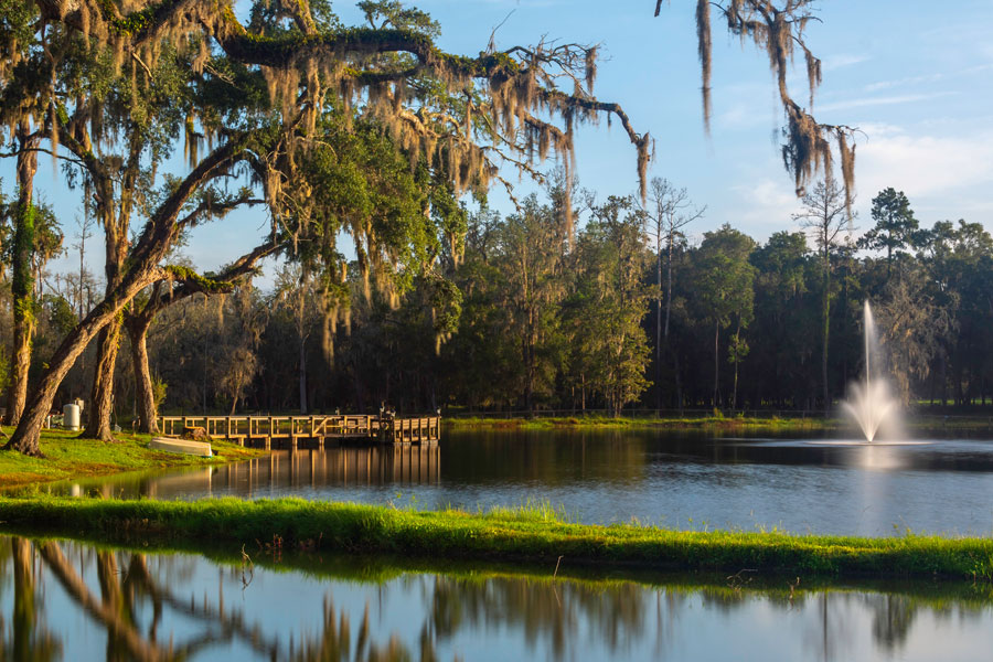 The dock and fountain at Belle Parc, framed by overhanging trees on the west bank of the lake at Belle Parc RV Resort, a 270-site on US 41 in central Florida. Brooksville, FL