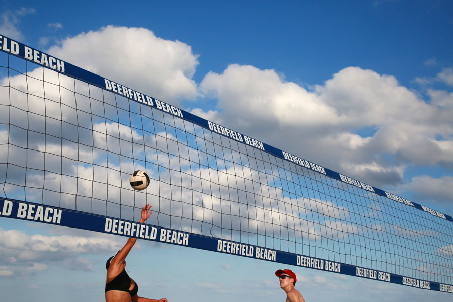 Young women play volleyball near the labelled net in a bright sunny afternoon with scattered clouds. Deerfield Beach, Florida, January 13 2018.