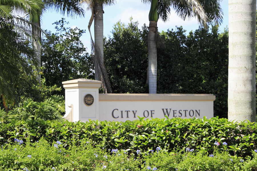 Entrance sign to the city of Weston, Florida, located in western Broward County, with beautiful flowers in front and tropical foliage behind on a sunny day