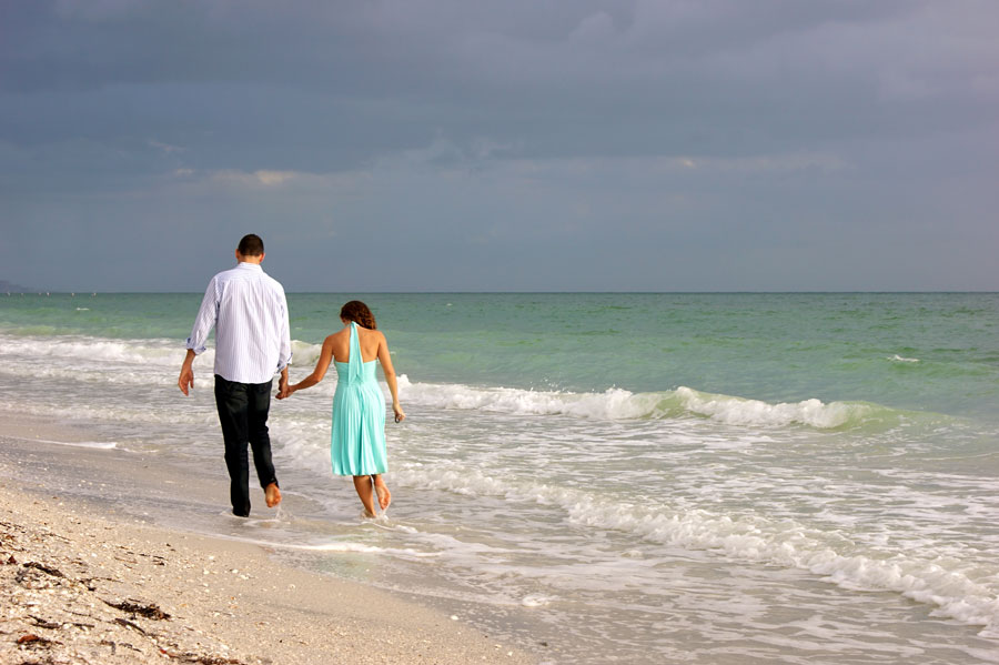 Young couple walking along Bonita Beach in Bonita Springs Florida on the gulf of Mexico as the sun begins to set behind them.