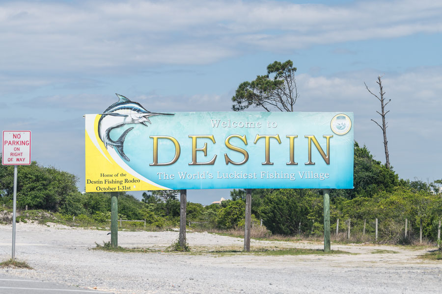 Road sign and billboard with Welcome to Destin the World's luckiest fishing village in Florida Panhandle. Destin, Florida on April 24, 2018.