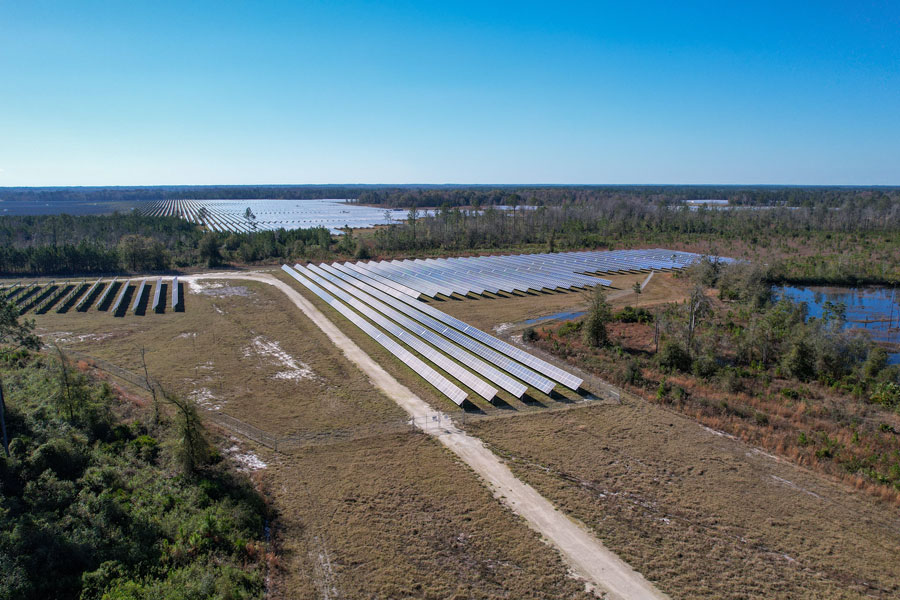 Noon time Aerial drone view over solar farm collecting green renewable energy for small rural town of Lake Butler Florida in dense forest.