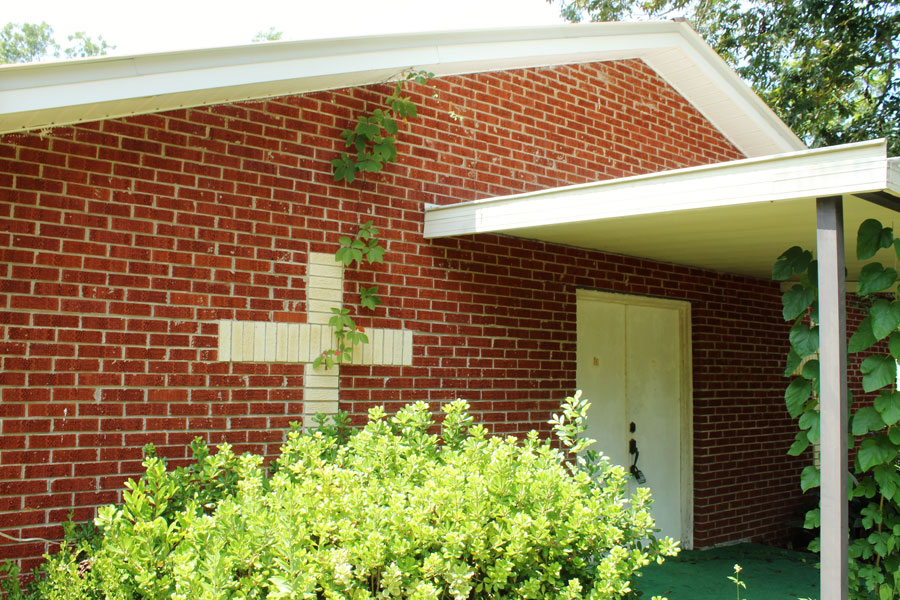 A white tiled cross on brick wall of church with white door in Bonifay, Florida. 